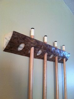 four wooden mallets hang on the wall with white pegs and one piece of wood sticking out of it