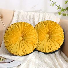 two yellow pillows sitting on top of a bed next to a plant in a vase