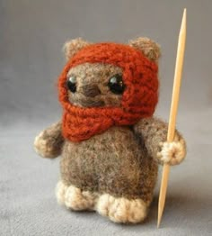 a small stuffed animal with a red scarf on it's head holding a wooden stick