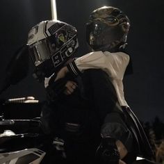 two people wearing helmets and standing next to each other in front of a motorcycle at night