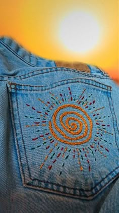 the back of someone's jean pants with an embroidered design on it, in front of a sunset