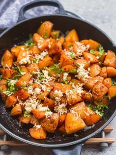 a skillet filled with cooked sweet potatoes and parmesan cheese on top, next to wooden chopsticks