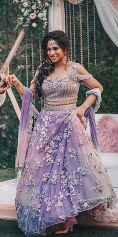 a woman in a purple and silver dress standing next to a bed with flowers on it