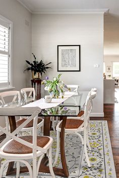 a dining room table with white chairs and a rug on the floor in front of it