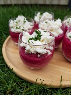 four glasses filled with food sitting on top of a wooden platter in the grass