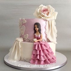 a pink and white cake with a doll sitting on top of it next to a rose