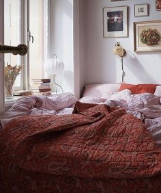 a bedroom with pink walls and pictures on the wall above the bed, along with an unmade red bedspread