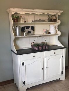 an old white hutch with pots and pans on the top, in a kitchen