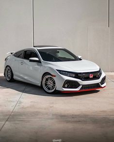 a white car is parked in front of a gray wall and cement floored area