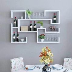 a dining room table with plates and wine glasses on the shelves above it, along with two vases filled with flowers