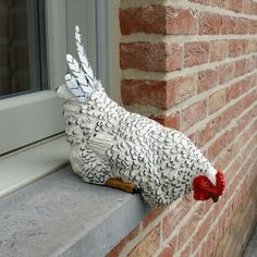 a white chicken statue sitting on top of a window sill next to a brick building