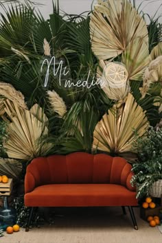 an orange couch sits in front of a backdrop with palm leaves and other tropical plants