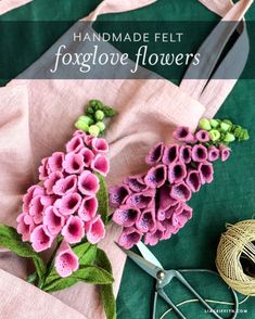 pink flowers are sitting on top of a piece of fabric next to scissors and yarn