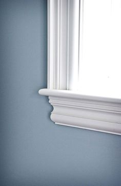 a white toilet sitting next to a window in a blue room with molding on the walls