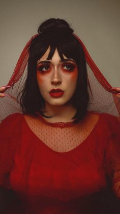 a woman with black hair and red makeup is wearing a veil over her head while posing for the camera