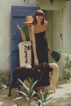 a woman standing next to a dog in front of a blue door with a straw hat on it's head