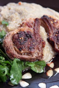 two pieces of meat on top of mashed potatoes with greens and garnishes