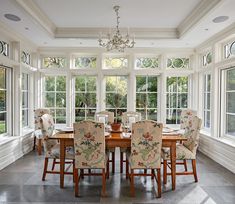 a dining room table and chairs in front of two large windows with chandeliers