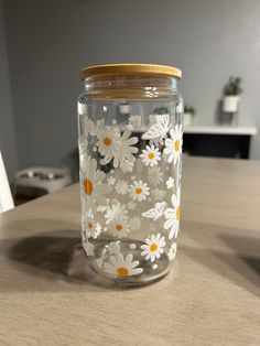 a glass jar with white and yellow flowers painted on the lid sitting on a table