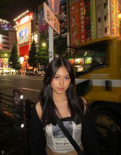 a young woman standing in front of a street sign at night with neon signs behind her