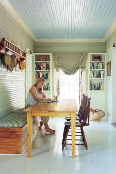 a woman sitting at a wooden table in front of a book shelf filled with books