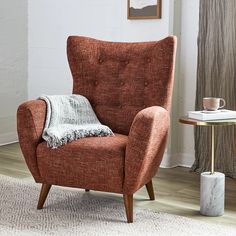 a chair with a blanket on it next to a side table and a vase in the corner