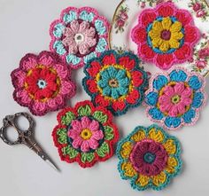 several crocheted flowers are sitting next to a pair of scissors