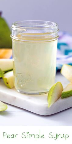 pear simple syrup in a glass jar on a cutting board with sliced apples and limes