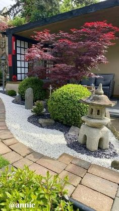 a small garden with rocks and trees in the background, along with a stone path leading to a building