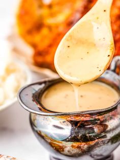 a wooden spoon pouring sauce into a small silver bowl with other dishes in the background