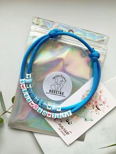 two bracelets on top of a bag with a tag attached to it and some flowers in the background