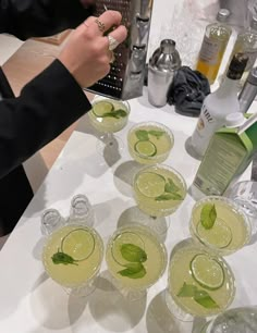 several glasses filled with green drinks on top of a white table next to bottles and silverware