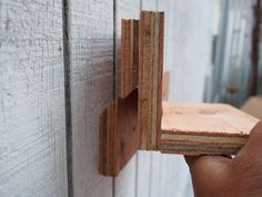 a person is holding some wood in front of a white wall with wooden boards on it