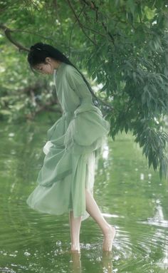 a woman in a green dress is standing in the water and looking down at her shoes