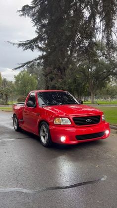 a red pick up truck parked in a parking lot next to some trees and grass