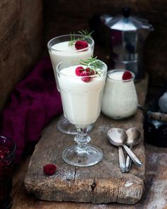 two glasses filled with pudding sitting on top of a wooden table next to spoons