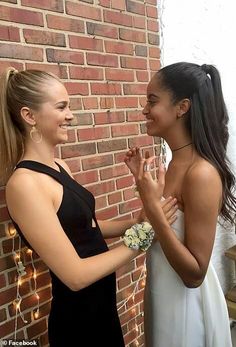 two women standing next to each other in front of a brick wall with string lights