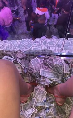 a person sitting on top of a bed covered in lots of dollar bills and wearing red shoes