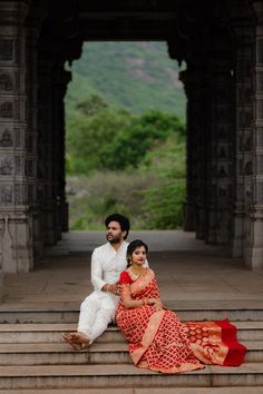 a man and woman sitting on steps in front of an archway with mountains in the background