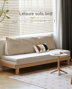 a white couch sitting in front of a window next to a table with a cup on it