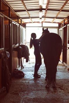 a woman standing next to a horse in a stable