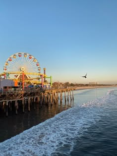 an amusement park with a ferris wheel on the water and a plane in the sky