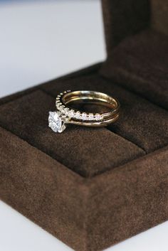 two wedding rings sitting on top of a brown velvet ring box, with one diamond set in the middle