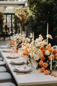 a long table is set with white and orange flowers