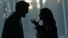 two people standing in front of a window with the sun shining through them and talking to each other