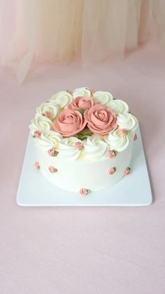 a white cake with pink frosting roses sitting on top of a white platter