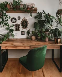 a wooden desk topped with lots of plants next to a green chair and wall mounted clock