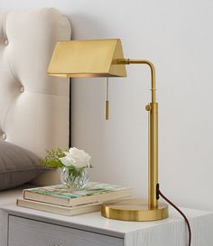 a gold lamp on a nightstand next to a book and vase with white flowers in it