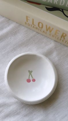 a bowl with cherries painted on it next to a book