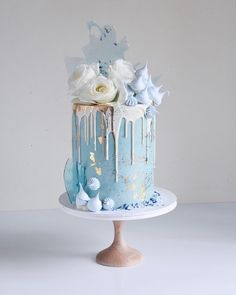 a blue cake with white flowers and icing on it sitting on top of a table